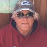 man with white hair peeking out from under a Greenbay Packers cap wearing aviator sunglasses and a red Cabela's hoodie.