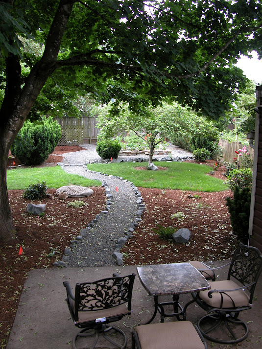 Backyard with stone bordered path and reduced lawn area. In progress